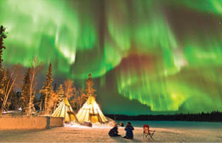 Aurora Village in Yellowknife, Canada is a popular destination to see the Northern Lights up close  The camp s glowing teepees complement the colorful ribbon of lights above 